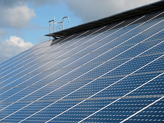 Blue solar panels on a roof against a cloudy sky