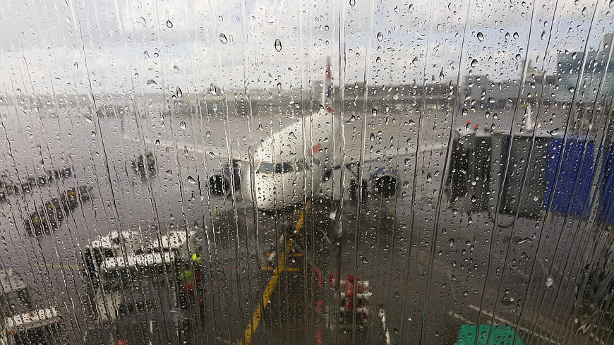 Airplane parked on tarmac viewed through rain-streaked airport window