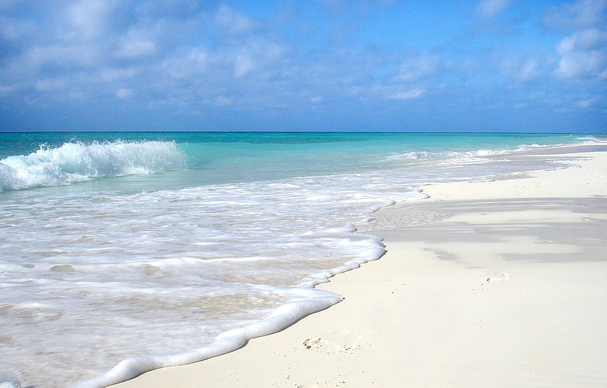 Turquoise Caribbean waves crashing on white sandy beach