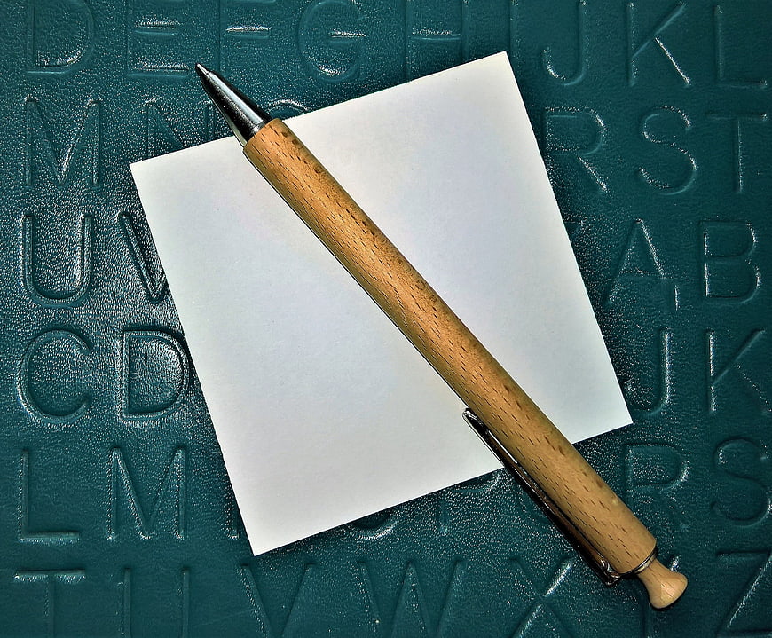 Wooden Pen On Blank Note Over Embossed Alphabet Background