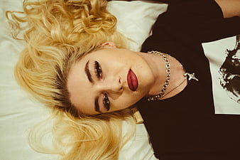 Blonde woman lying on bed with red lipstick and silver jewelry