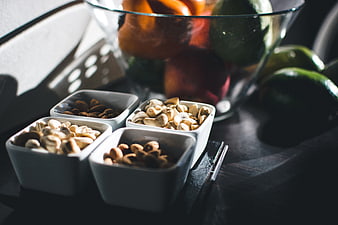 Assorted Nuts in White Bowls with Fruit Background