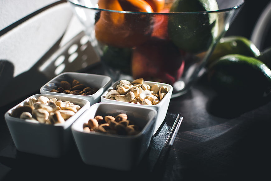 Assorted Nuts in White Bowls with Fruit Background