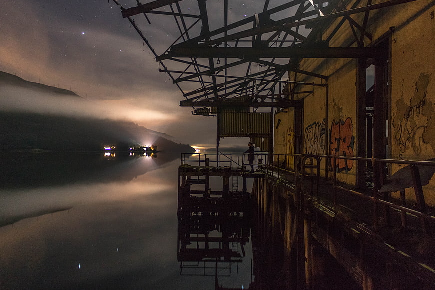 Lone figure on industrial dock under starry night sky