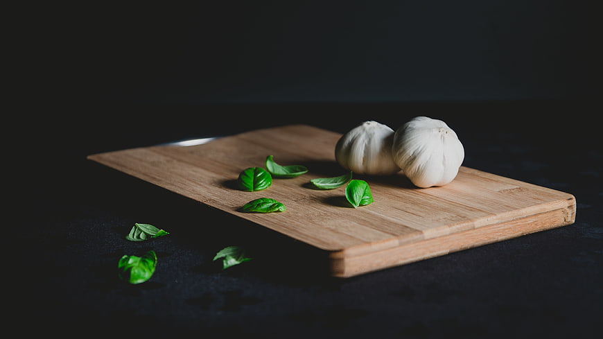 Garlic bulbs and fresh basil leaves on a wooden cutting board