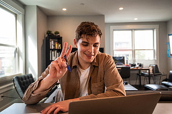 Young man making peace sign while working on laptop at home