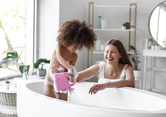 Happy mother and toddler playing with bubbles in bathtub