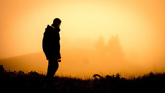 Silhouette of Man Standing in Orange Foggy Landscape