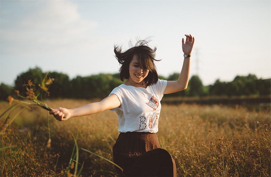 Happy woman dancing in a sunny field with wildflowers