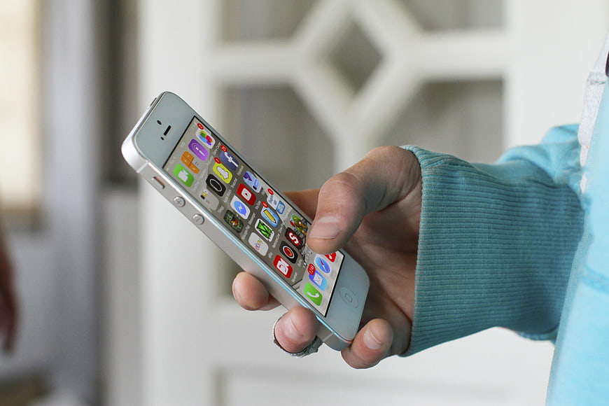 Hand holding white smartphone with app icons on screen