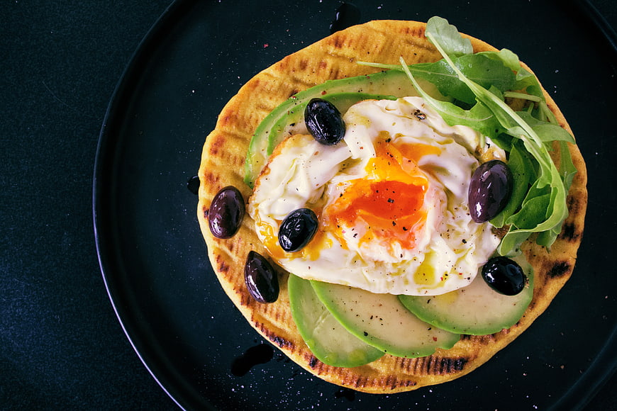 Overhead shot of avocado toast with fried egg and olives
