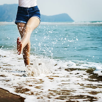 Barefoot woman splashing in ocean waves on sandy beach