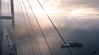 Cable-stayed bridge in fog with cargo ship at sunrise