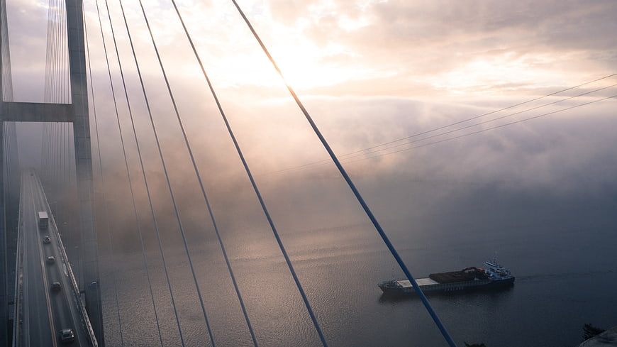 Cable-stayed bridge in fog with cargo ship at sunrise
