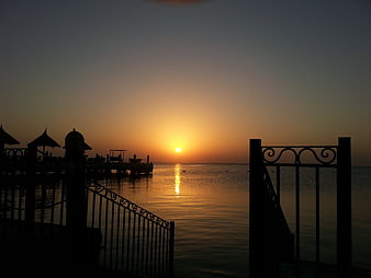 Silhouette of pier and gate at sunset over calm sea