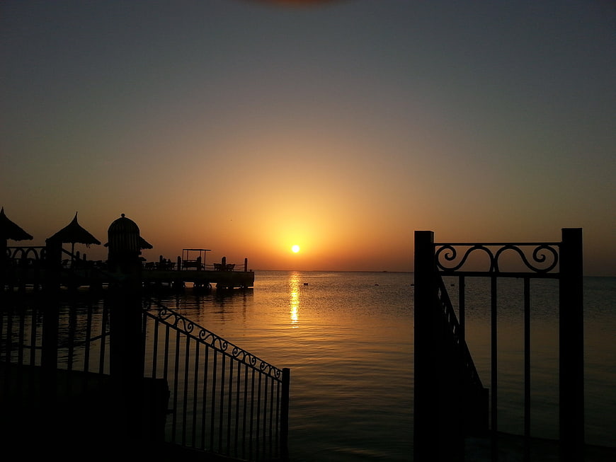 Silhouette of pier and gate at sunset over calm sea