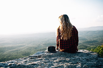 Woman in plaid shirt sitting on rocky mountain overlook