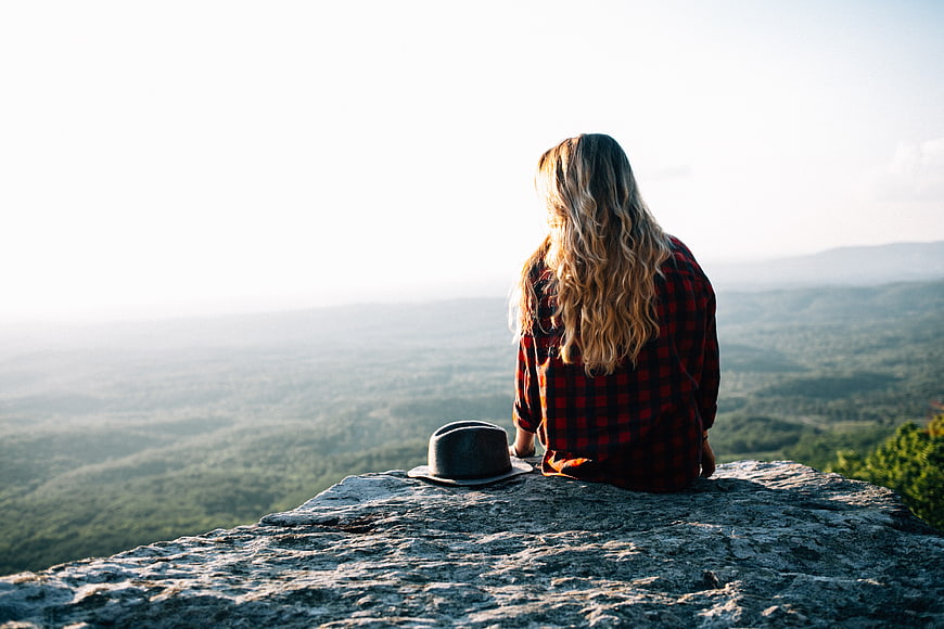 Woman in plaid shirt sitting on rocky mountain overlook