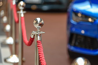 Red velvet rope barrier with chrome stanchion and blurred blue car