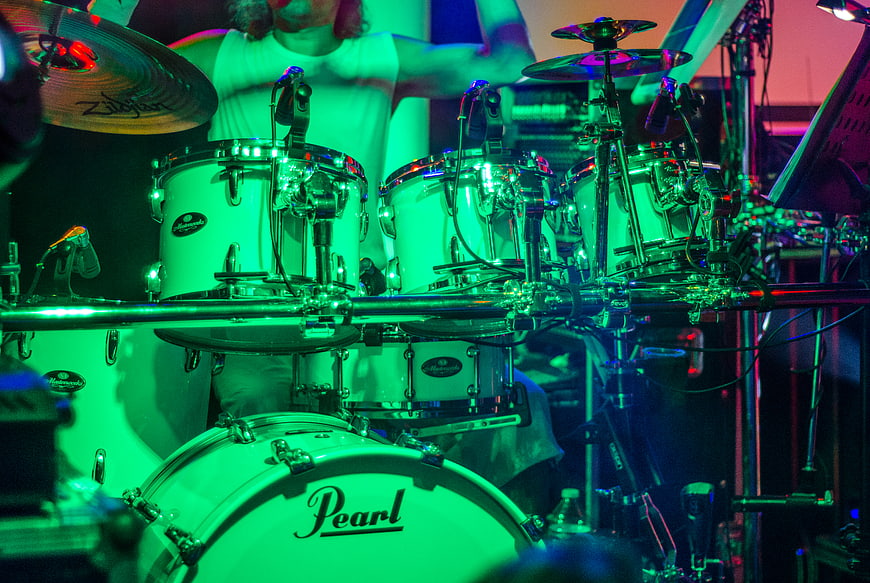 Drummer performing on stage with green and blue lighting