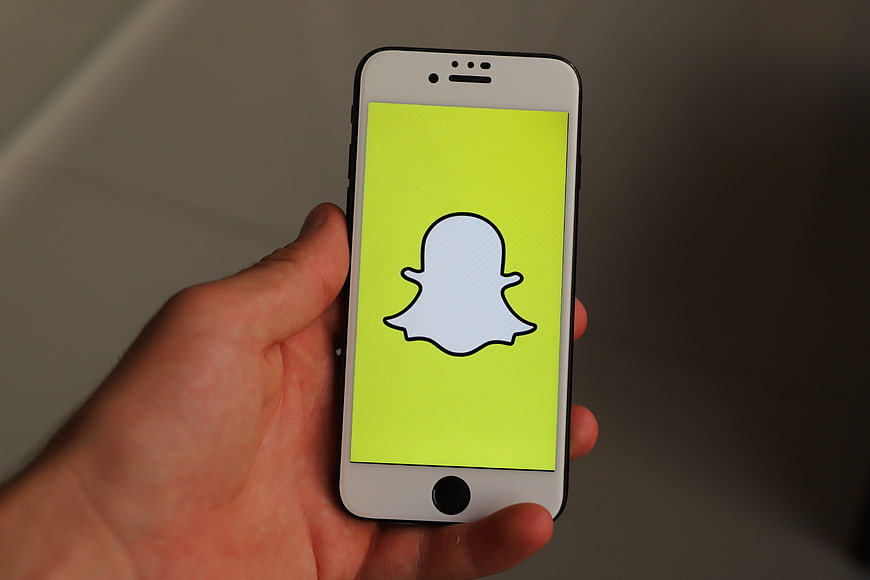 Hand Holding White Smartphone Displaying Snapchat App Icon