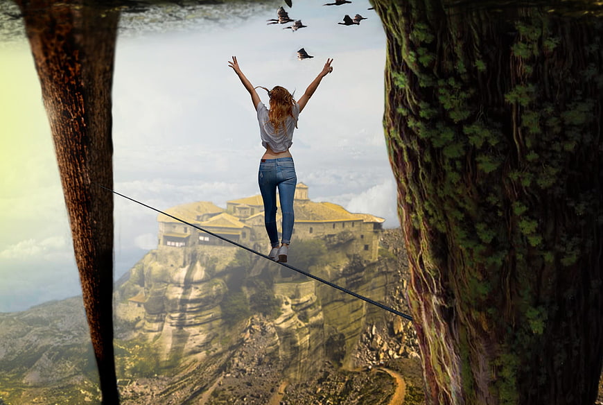 Woman walking tightrope between trees with mountain monastery background