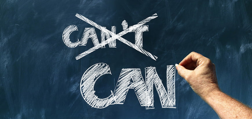 Hand writing CAN on chalkboard crossing out CAN'T motivational concept