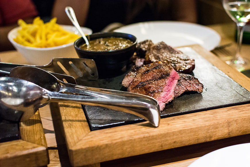 Grilled medium-rare steak on wooden board with fries and sauce
