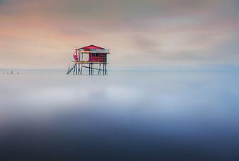 Lonely stilt house on misty sea at sunset
