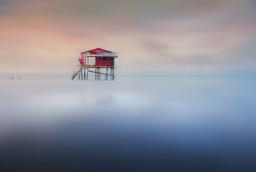 Lonely stilt house on misty sea at sunset