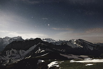 Snowy mountain range under starry night sky with moon
