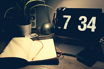 Laptop with Digital Clock and Open Notebook on Desk