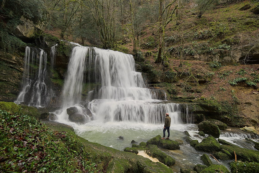 Man standing on rocks near a cascading waterfall in a forest