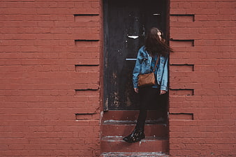 Woman in Denim Jacket Standing by Red Brick Wall
