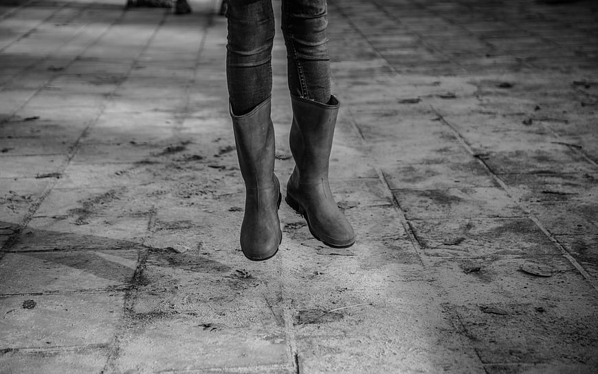 Black and white photo of woman's rain boots on pavement