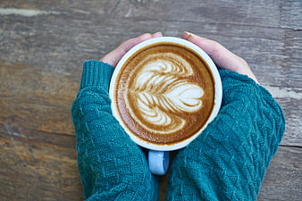 Hands holding latte art coffee in teal sweater