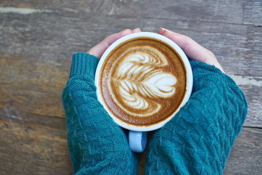 Hands holding latte art coffee in teal sweater