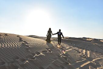 Happy couple holding hands walking on sand dunes