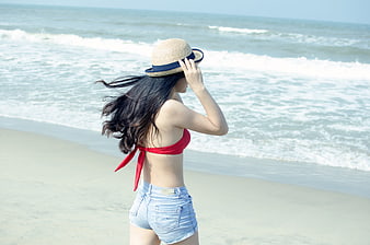 Young woman in red bikini top and denim shorts on beach