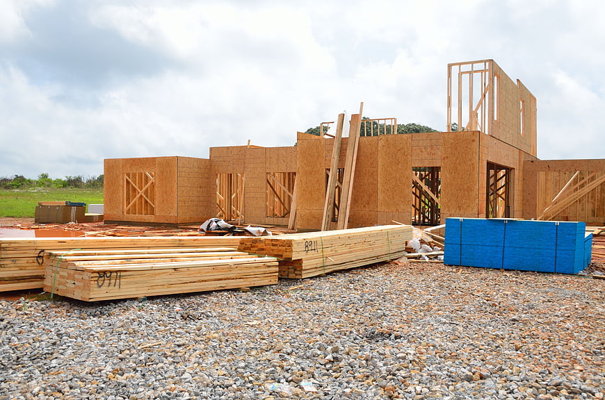 Wooden house frame under construction with lumber stacks