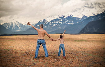 Father and son holding hands in a field facing snowy mountains