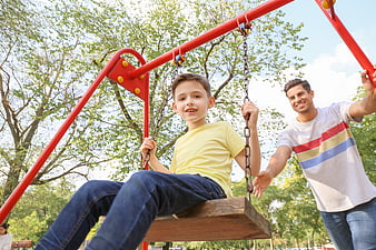 Happy Father Pushing Son on Swing in Park
