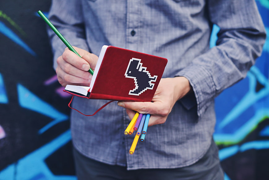 Man holding red pixel art notebook and colored pencils