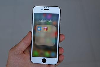 Hand holding white smartphone displaying social media app folder