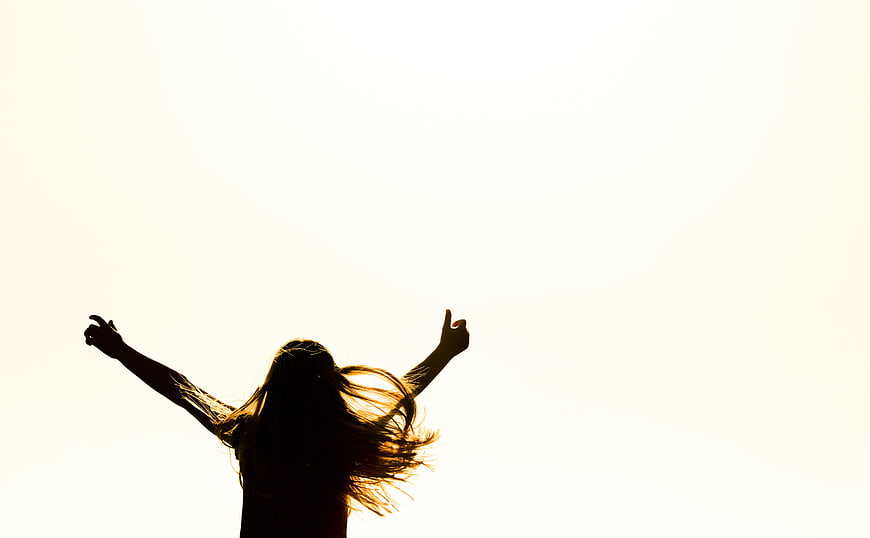 Silhouette of woman with arms raised in joy against bright sky