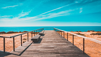 Wooden boardwalk leading to ocean with benches and blue sky