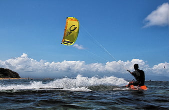Kitesurfer riding waves on sunny blue ocean day