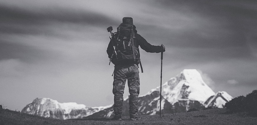 Hiker with Backpack and Poles Facing Snowy Mountain Peak