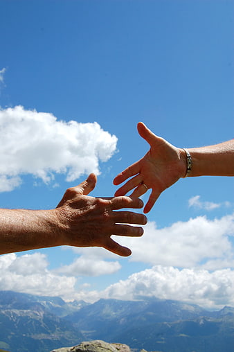 Two Hands Reaching Out Against Blue Sky and Mountains