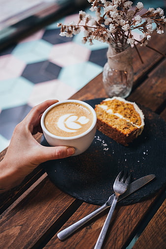Hand holding latte with cake on wooden table